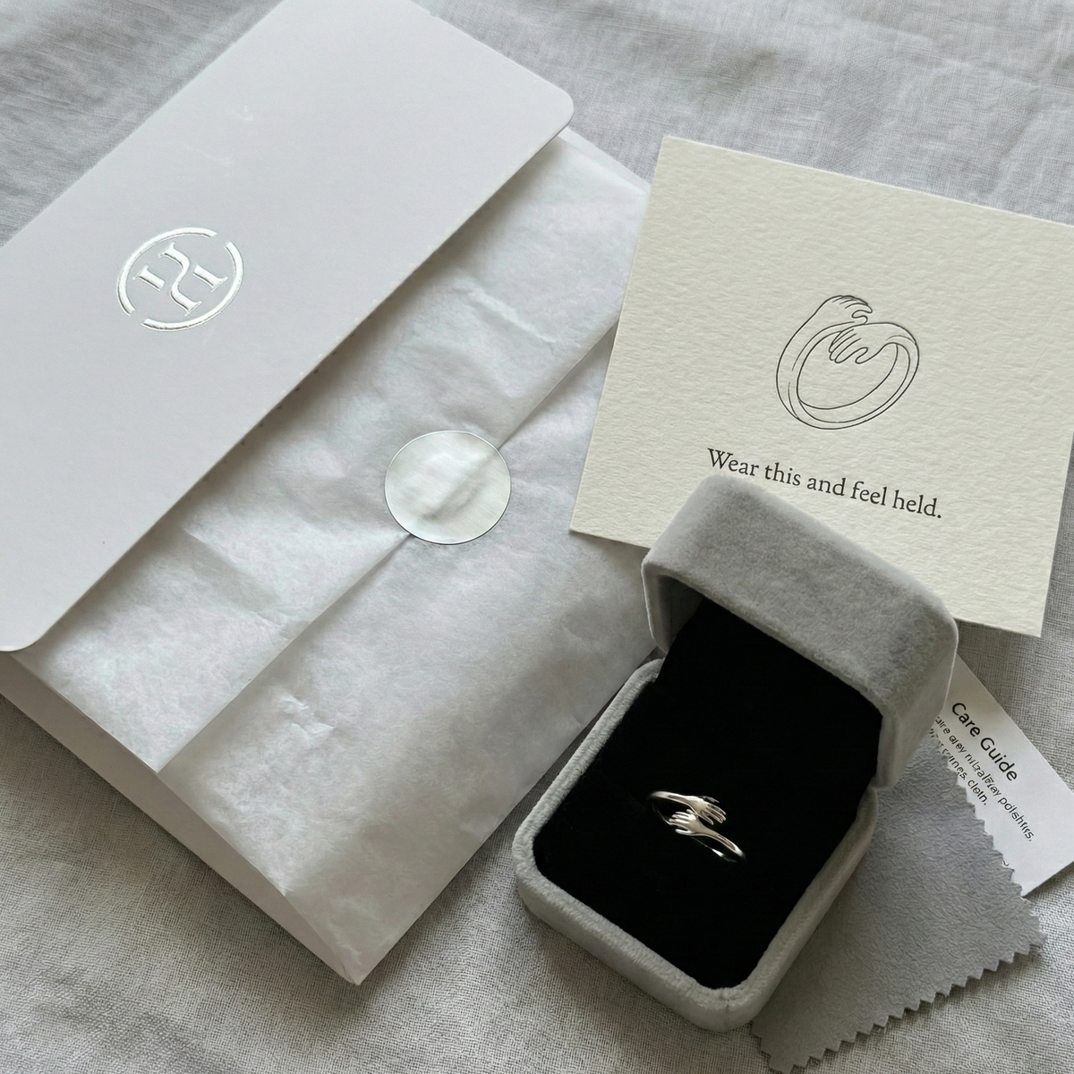 Silver ring in a box with a card and tissue paper on a gray surface