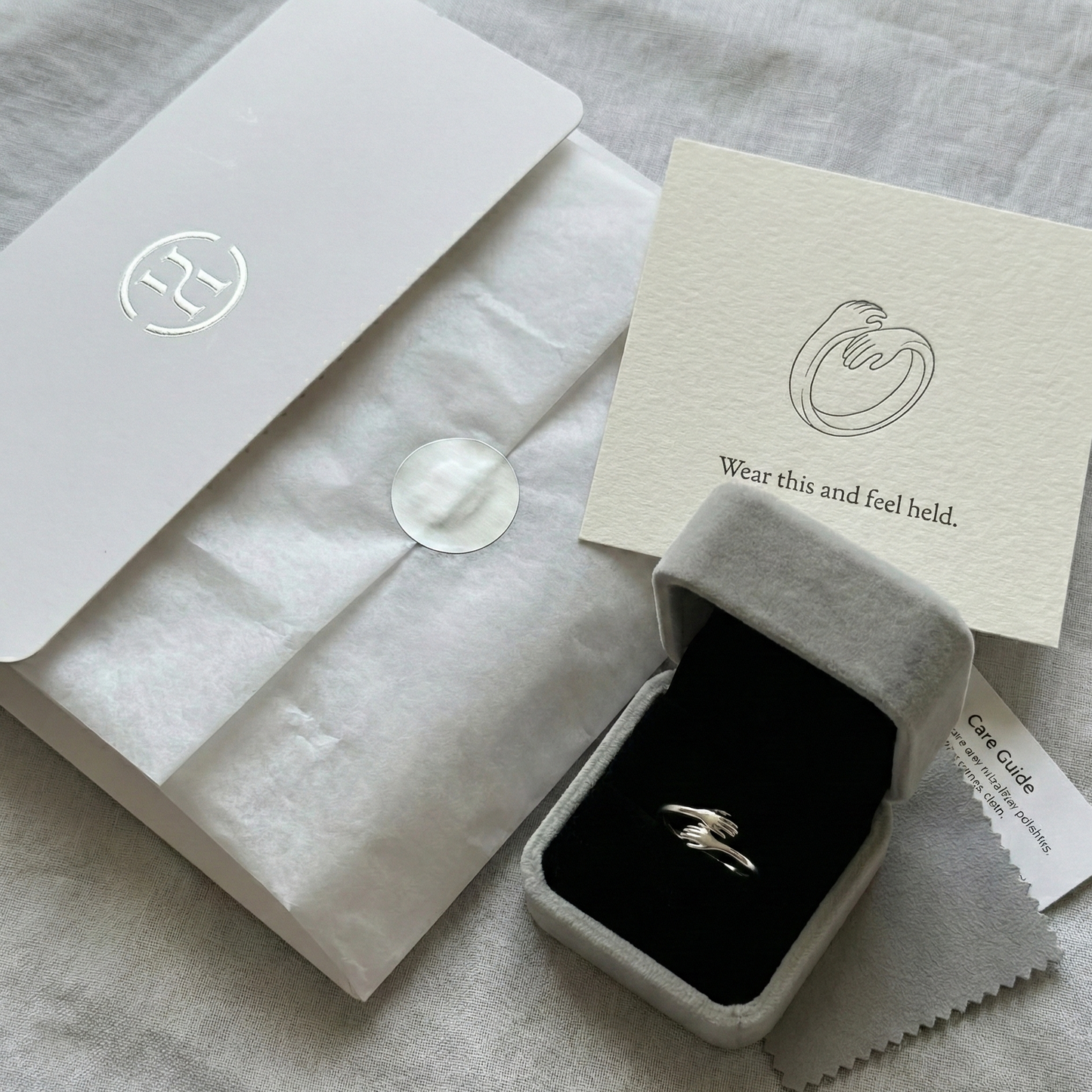 Silver ring in a box with a card and tissue paper on a gray surface